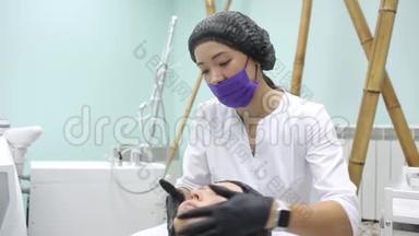 戴着刷子的粉<strong>红色</strong>手套的美容师用一个碳<strong>面膜</strong>在一个年轻女孩的脸上剥皮